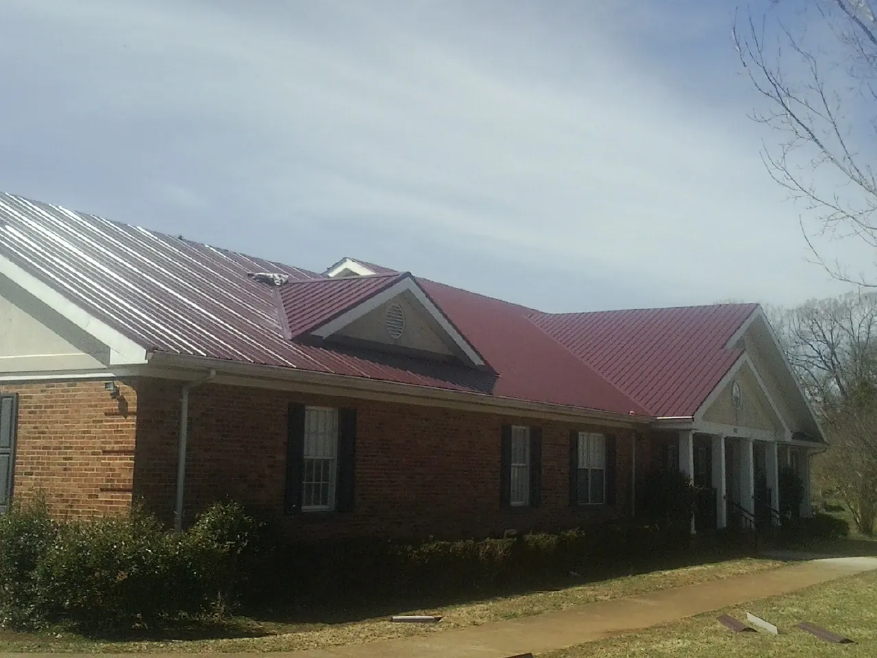 Red metal roof with gabled entries on a long brick building, from a Hail Damage Roof Repair job in Hitterdal