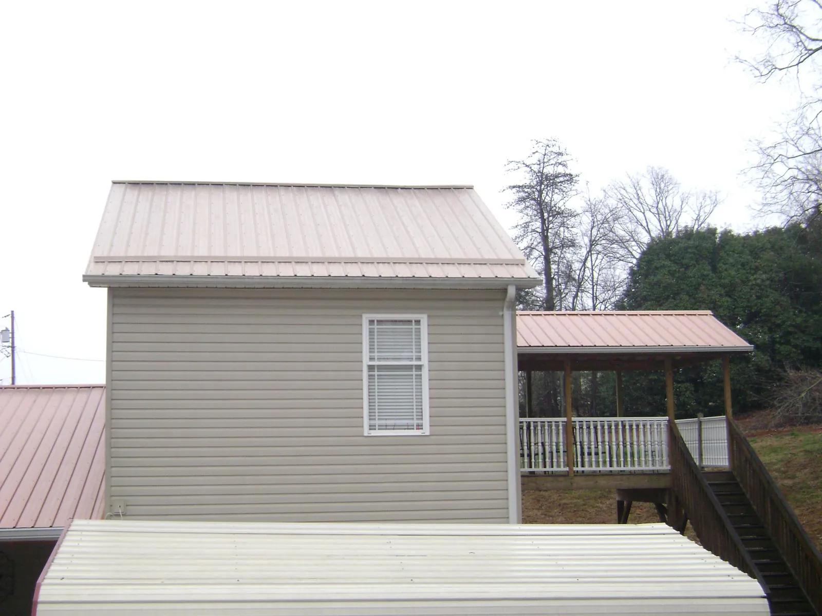 Tan metal roofs on a two story addition and attached porch, from a Roof Replacement job in Hitterdal